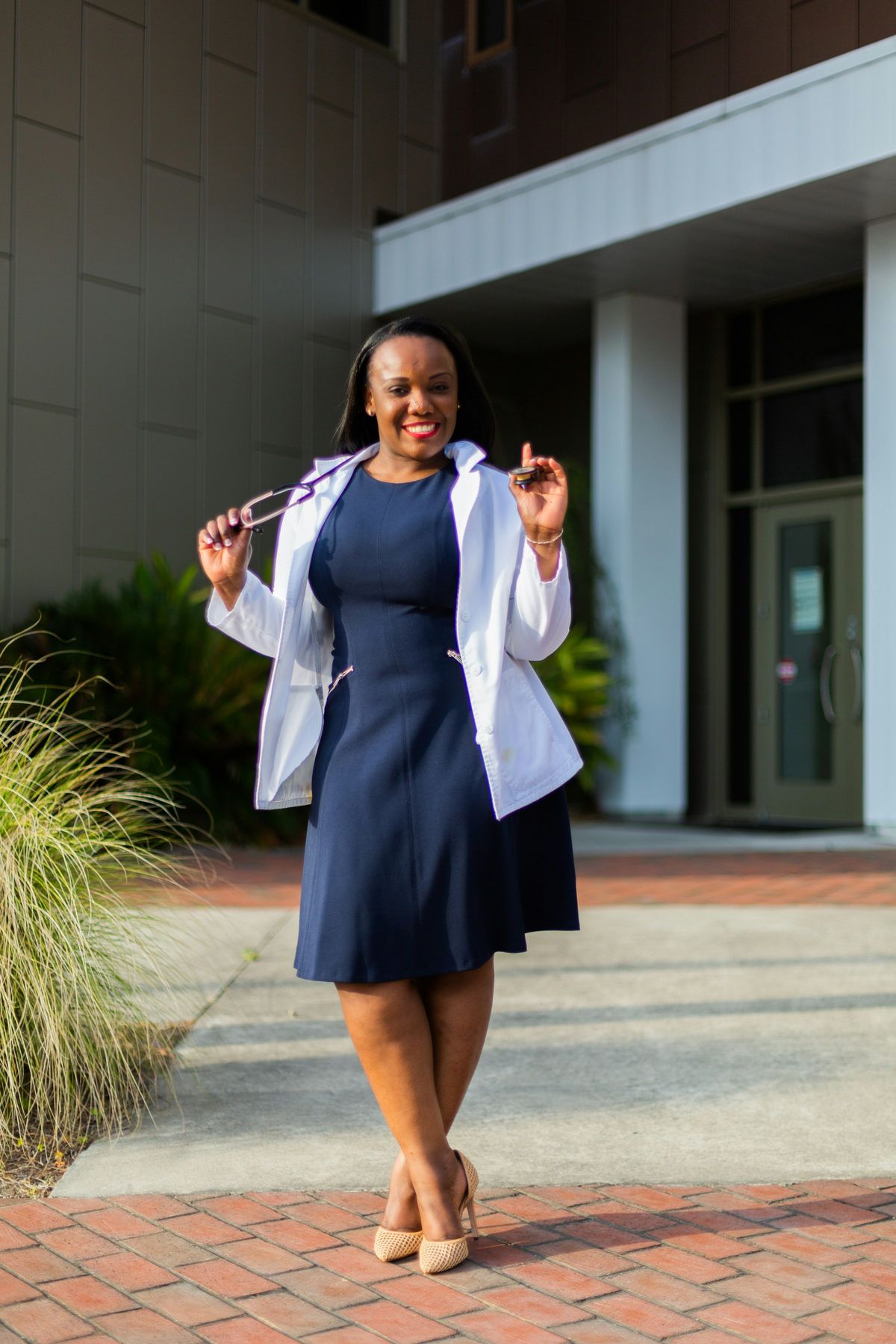 A smiling young woman in a white coat standing outside a building